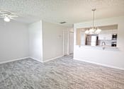 Thumbnail 7 of 15 - an empty living room with a kitchen and a ceiling fan