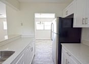 Thumbnail 9 of 15 - an empty kitchen with white cabinets and a black refrigerator