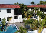 Thumbnail 20 of 21 - A white building with a red roof and a pool surrounded by palm trees.