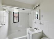 Thumbnail 27 of 49 - A white bathroom with a tub, sink, mirror, and a window.