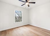 Thumbnail 17 of 31 - A room with a ceiling fan and a window with a view of trees.