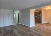 Thumbnail 3 of 16 - A room with wood flooring and a kitchen in the background.