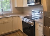 Thumbnail 11 of 17 - A kitchen with white cabinets and a black microwave above the stove.