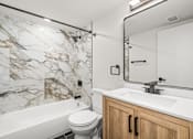 Thumbnail 14 of 31 - A white and marble bathroom with a toilet, sink, and bathtub.