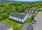 Thumbnail 26 of 30 - A white house with a black roof is surrounded by greenery and a parking lot.