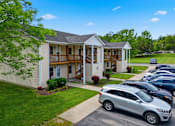 Thumbnail 28 of 30 - A silver car is parked in a lot in front of a two-story building with a covered porch.
