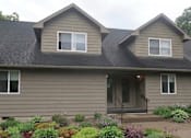 Thumbnail 9 of 15 - A house with a grey roof and a grey wall with a small garden in front.