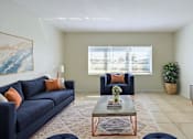 Thumbnail 4 of 25 - A living room with a blue couch, a coffee table, and a painting on the wall.