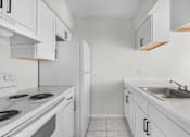 Thumbnail 3 of 14 - A white kitchen with a stove, sink, and cabinets.