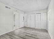 Thumbnail 10 of 14 - A room with white walls and wood flooring with a door on the left and three closets on the right.