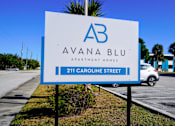 Thumbnail 11 of 12 - A sign for Avana Blu Apartment Homes is displayed in front of a building.