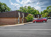 Thumbnail 27 of 29 - A red car is parked in a parking lot in front of a building.
