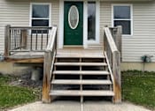 Thumbnail 31 of 53 - A house with a green door and a wooden staircase leading to it.