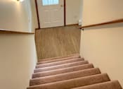Thumbnail 8 of 53 - A staircase with a brown carpeted runner and white walls.
