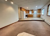 Thumbnail 14 of 53 - A spacious room with a kitchen area in the background.