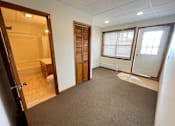 Thumbnail 26 of 53 - A room with a carpeted floor, a toilet visible through the open door, and a window with blinds.