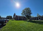 Thumbnail 27 of 38 - A sunny day at a grassy parking lot with cars and a building in the background.