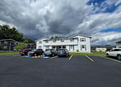 Thumbnail 21 of 22 - A parking lot with cars and a white building in the background.