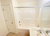 Thumbnail 16 of 30 - A white bathroom with a tub, sink, and mirror.