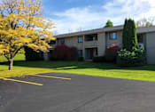 Thumbnail 14 of 18 - A parking lot in front of a building with trees and bushes.