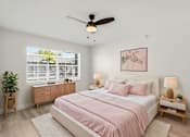 Thumbnail 4 of 26 - A bedroom with a pink bedspread and a ceiling fan.