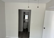 Thumbnail 12 of 23 - A room with a ceiling fan and a doorway leading to another room.