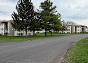 Thumbnail 32 of 38 - A road in front of apartment buildings with trees on the side.