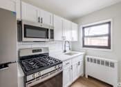 Thumbnail 1 of 49 - A white kitchen with a stove, oven, microwave, and refrigerator.