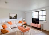 Thumbnail 36 of 49 - A living room with a white couch, orange pillows, a pink coffee table, and a flat screen TV.