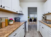 Thumbnail 1 of 18 - A kitchen with white cabinets and a brown countertop.