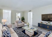Thumbnail 2 of 18 - A living room with a white couch, a coffee table, and a TV on a cabinet.