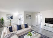Thumbnail 4 of 12 - A living room with a white couch and a glass coffee table.