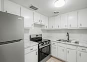 Thumbnail 24 of 25 - A kitchen with white cabinets and a black refrigerator.