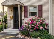 Thumbnail 22 of 26 - A small house with a black door and a flower bed in front.