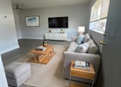Thumbnail 19 of 21 - A living room with a white couch and a wooden coffee table.