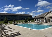 Thumbnail 42 of 55 - A swimming pool surrounded by sun loungers and a building in the background.