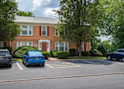Thumbnail 28 of 31 - A blue car is parked in a parking lot in front of a red brick building.