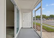Thumbnail 8 of 23 - A white door is open to a balcony with a view of a parking lot and trees.
