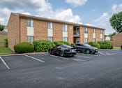 Thumbnail 13 of 19 - A black car is parked in a parking lot in front of a brick building.