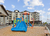 Thumbnail 6 of 32 - a playground with a swing set and slides in front of an apartment building