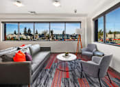 Thumbnail 9 of 25 - A living room with a grey couch, a grey chair, a round coffee table, and a large window with a view of the outside.