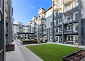 Thumbnail 5 of 46 - Apartment complex with a walkway and greenery in the foreground.