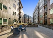Thumbnail 3 of 25 - A sunny day in a courtyard with a bench and a building in the background.