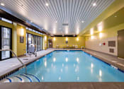 Thumbnail 5 of 32 - A large indoor swimming pool with a blue tiled edge.