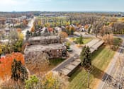 Thumbnail 3 of 31 - A large building sits in the middle of a grassy area with trees in the background.