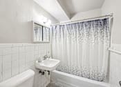 Thumbnail 19 of 39 - A white bathroom with a white tub, sink, and shower curtain.