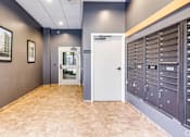 Thumbnail 52 of 52 - A hallway with a white door and a wall of mailboxes.