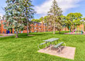 Thumbnail 10 of 34 - A green picnic table sits in a grassy area in front of a red building.