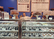 Thumbnail 52 of 68 - a man standing behind the counter of a display case of donuts