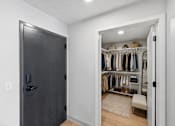 Thumbnail 5 of 54 - A black door is on the left of a room with a white wall and a white closet with clothes hanging on it.